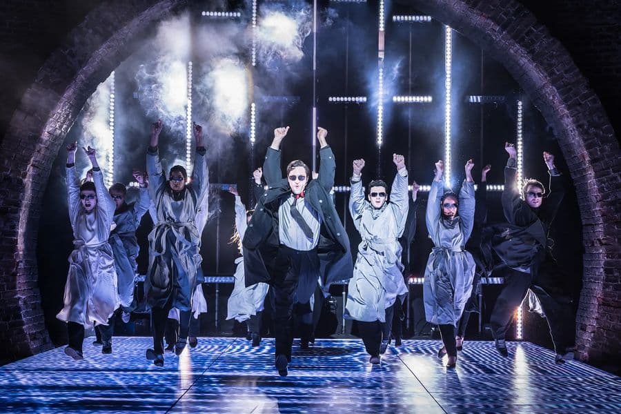 Groupe of people dance on stage wearing trench coats on stage in American Psycho at the Almeida Theatre