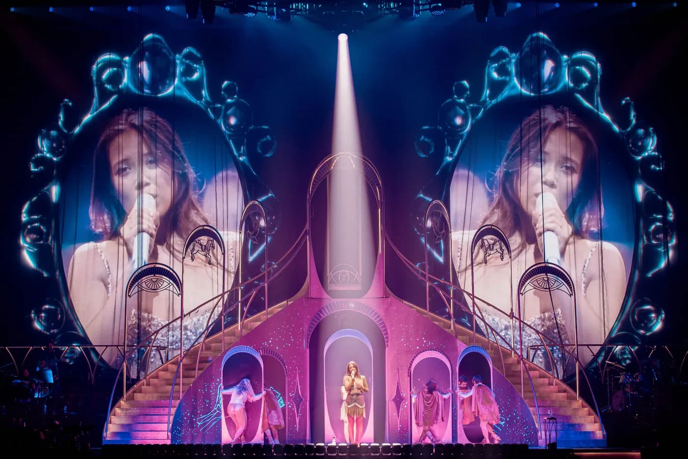 Laufey singing under spotlight with mirrored video projections on stage.