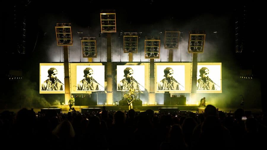 5 large led screen in black, white and yellow showing distorted footage of the band