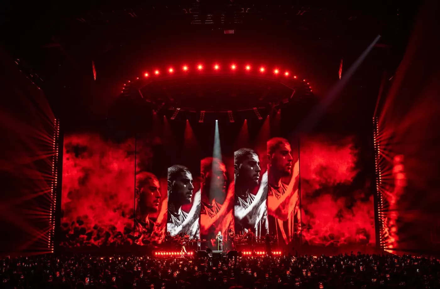 Zayn Malik performs under a sharp white spotlight, backed by a massive panoramic screen displaying five repeating, side-profile close-ups of him amidst billowing red smoke.