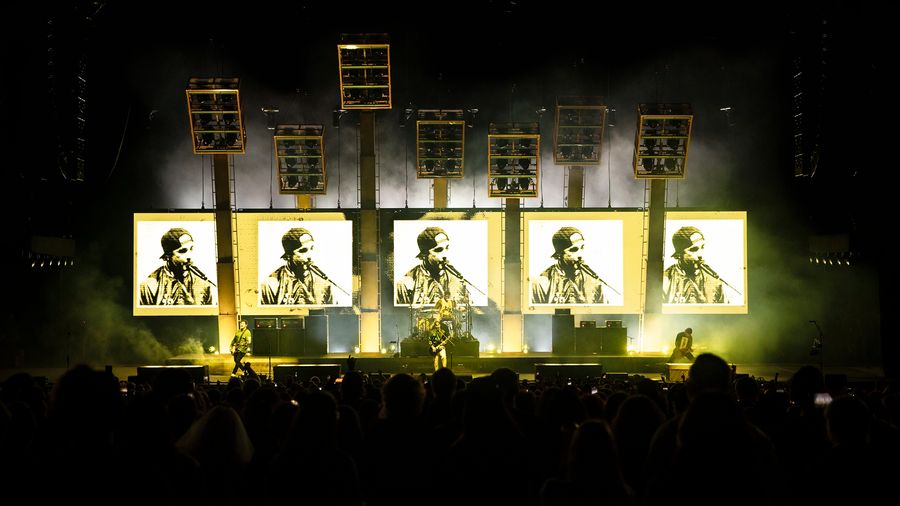 5 large led screen in black, white and yellow showing distorted footage of the band