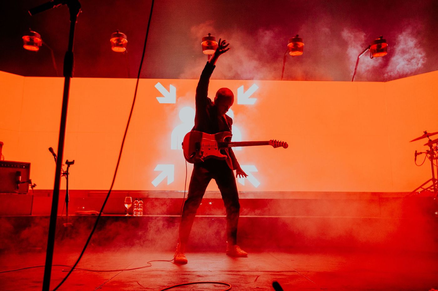 Guitarist’s silhouette cuts against bright red screen with graphic arrows, crafted by FRAY Studio.